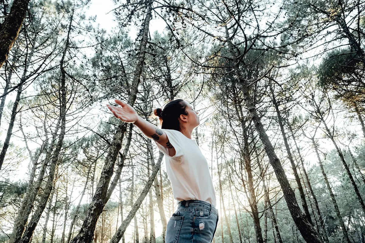 An image of a young women with her hands stretched feeling the nature.